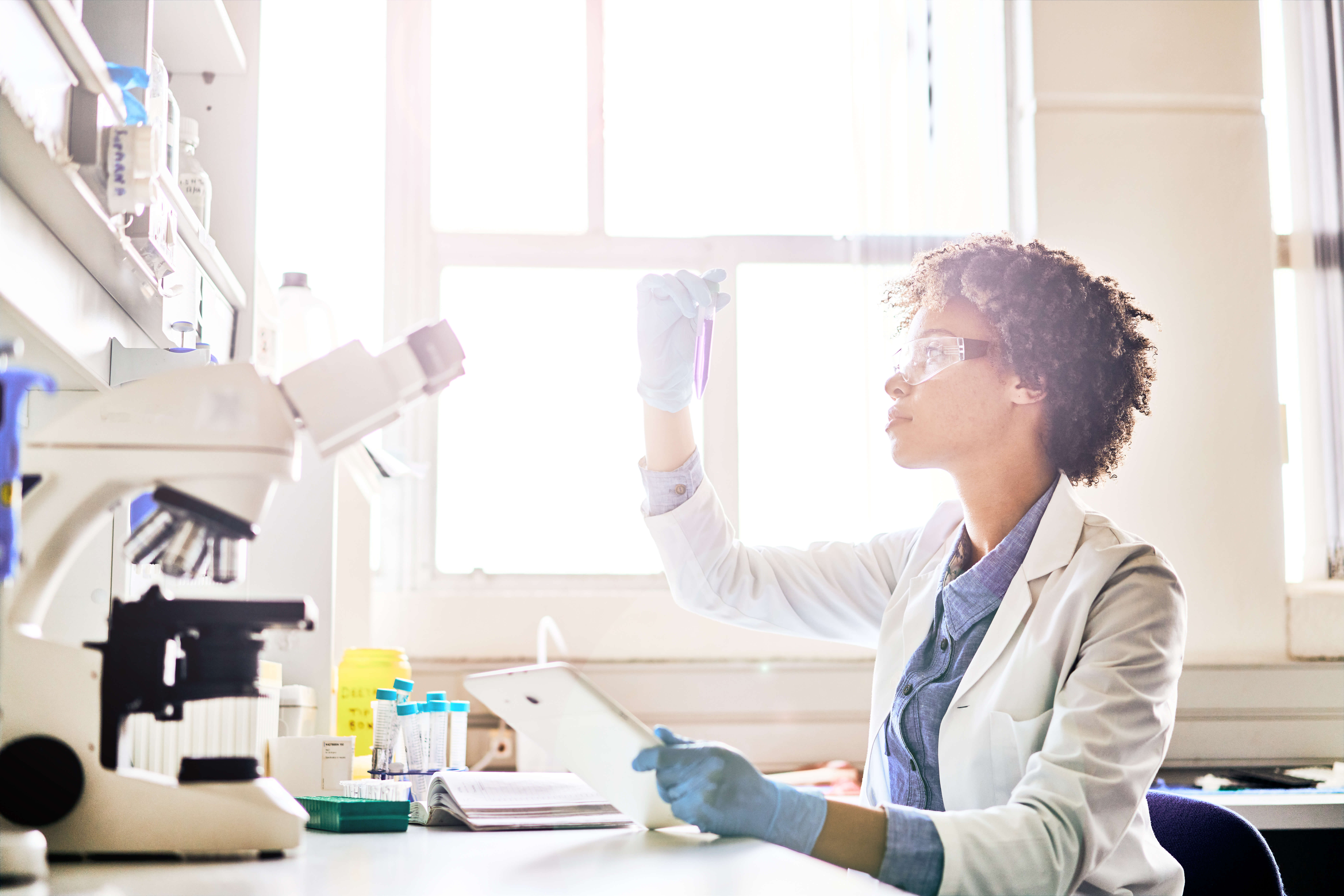 Young female scientist working on a digital tablet and examining a test tube sample while sitting at a table in a lab